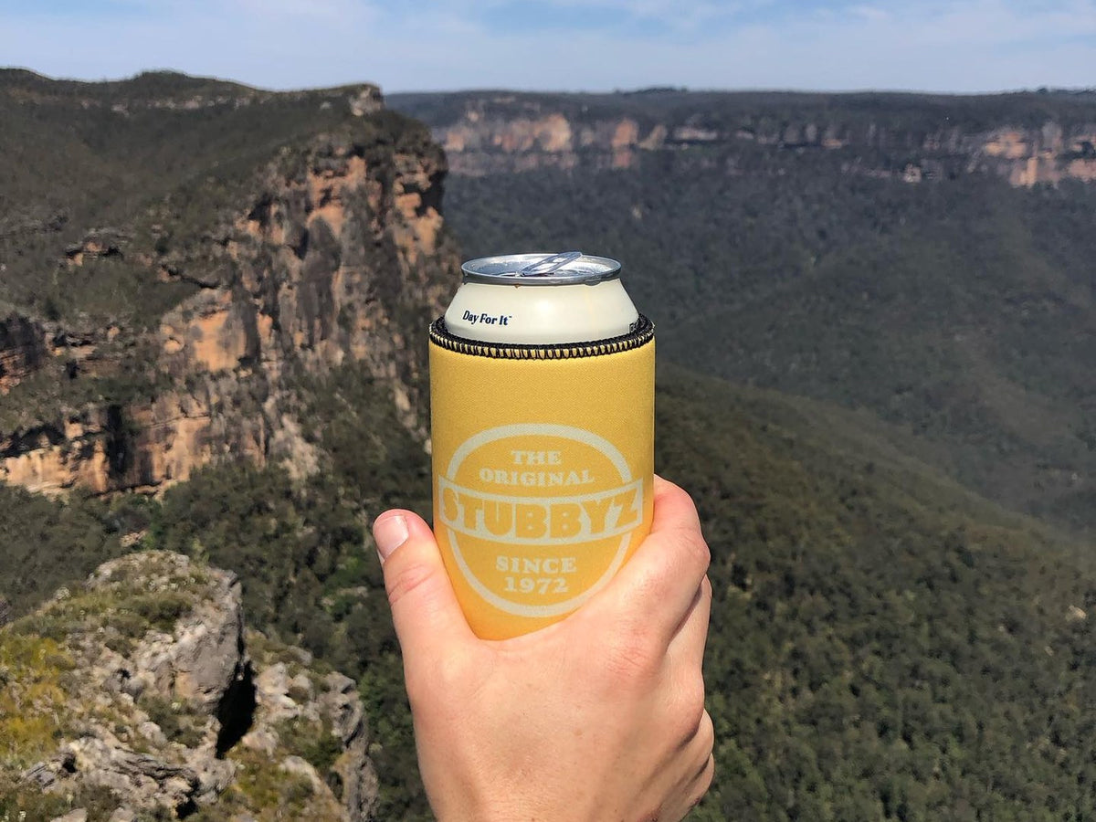 An Original Stubbyz stubby holder held up over the Blue Mountains
